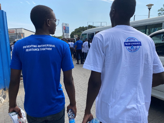 Two young men talking and wearing t-shirts that reads: Preventing antimicrobial resistance together and handle with care.