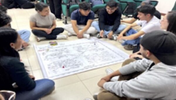 Group of students sitting on the floor around an educational board game.