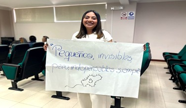 Smiling woman holds a sign about the importance of microbes in a classroom setting.