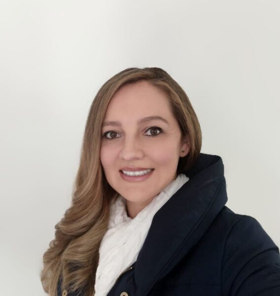 Jasmin Moyano, Project assistant of react Latin America poses against a white while, smiling. Dressed in a blue jacket.