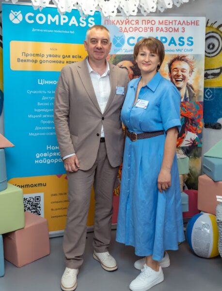 Alla Kuzhel stands with a male colleague in front of colourful COMPASS nursing education displays.