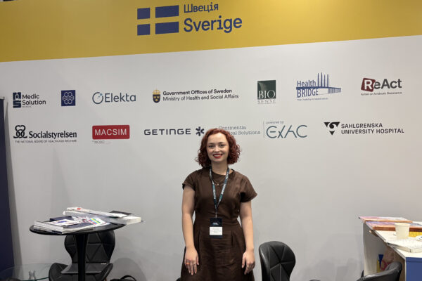 Marta Dumanska, ReAct Europe standing infront of a wall with logos of participating Swedish organizations.